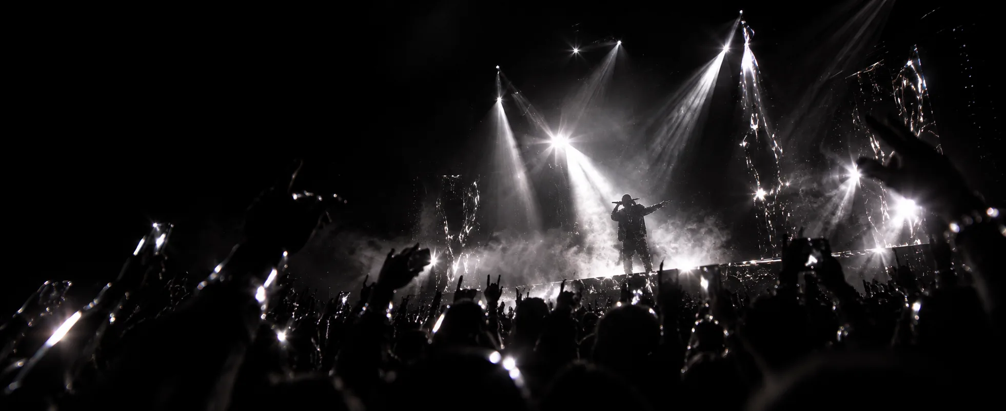 Concert crowd with raised hands facing a performer under bright stage lights